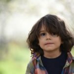 Portrait of a cute child with long hair wearing a plaid shirt, standing outdoors during spring.